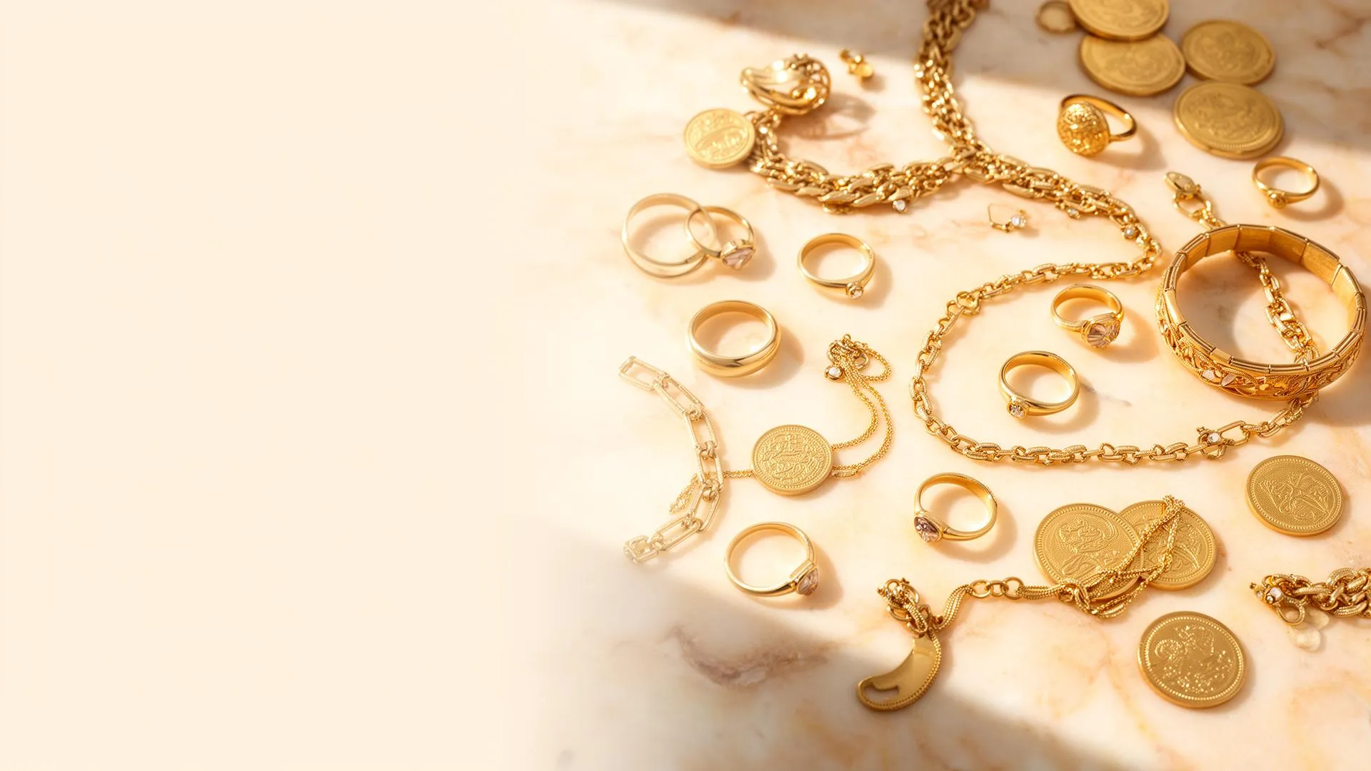Gold jewelry, rings, chains, and coins on a warm cream marble surface